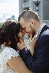 Young beautiful stylish pair of newlyweds hugs each other and stay face to face with smile on stairs.