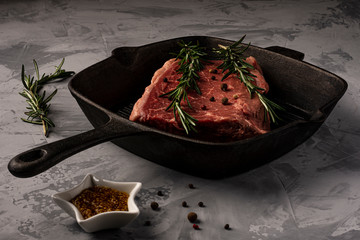 A piece of fresh marbled beef with sprigs of rosemary in a cast-iron grill pan, ready to cook.