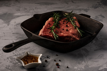 A piece of fresh marbled beef with sprigs of rosemary in a cast-iron grill pan, ready to cook.