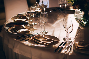served table with white tablecloth. white plates, wine glass, fork, knife - obrazy, fototapety, plakaty