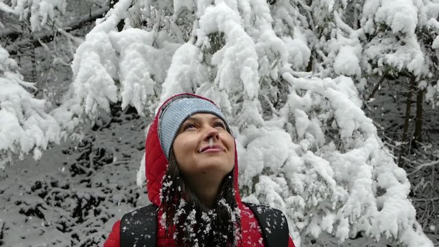 The girl rejoices in the snow in winter. Beautiful snowfall. Snow-covered trees in the forest.