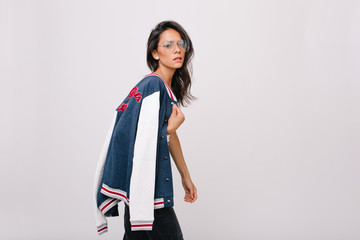 Worried brunette young woman in big glasses carrying colorful sport jacket on shoulder. Unhappy...