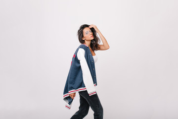 Wonderful dark-haired european lady in black jeans looking with tired face expression while posing on white background. Indoor portrait of stylish girl in glasses dancing in sport jacket.