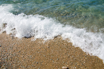 Summer background. Colorful coast with sea wave. View of the pebble beach and clear turquoise water