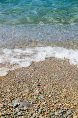 Summer background. Colorful coast with sea wave. View of the pebble beach and clear turquoise water