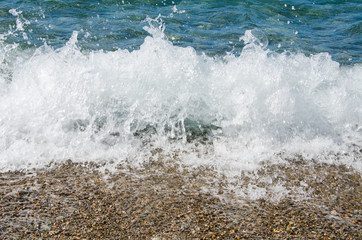 Summer background. Colorful coast with sea wave. View of the pebble beach and clear turquoise water