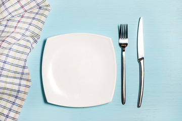 Fork, knife and empty plate near napkin in a cage on a blue wooden background.