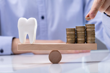 Stack Of Coins And Healthy Tooth On Seesaw