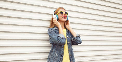 Cool girl in wireless headphones enjoying listening to music on city street over white wall background