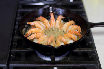 Shrimp cooking in butter and garlic in a cast iron skillet on the stove.
