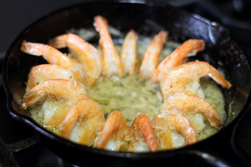 Shrimp cooking in butter and garlic in a cast iron skillet on the stove.