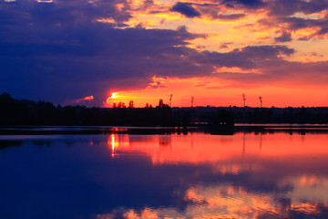 Fototapeta premium Dramatic sunset on the water with symmetry of colorful clouds cumulonimbus. Golden orange reflection of the sun's rays in a lake