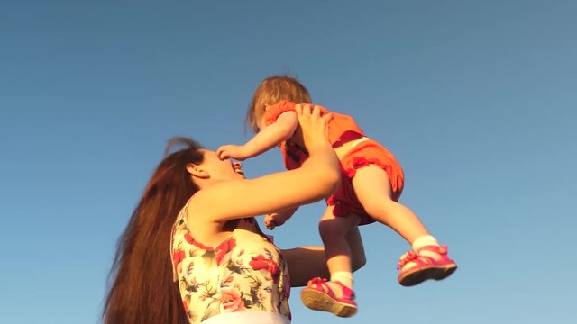 Mom throws her daughter up to the sky. mother plays with a small child against a blue sky. happy family playing in the evening against sky. mother throws up baby, baby smiles. slow motion filming.