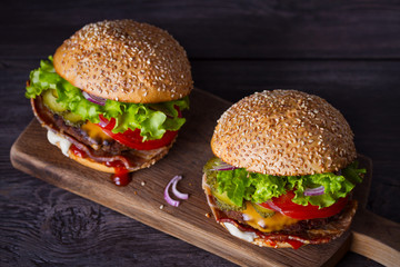 Delicious homemade beef burgers with bacon on wooden chopping board. horizontal