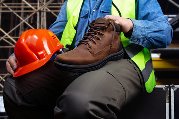 Worker sitting with suede boot footwear and protective helmet on construction background.