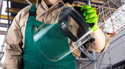 Worker in green overall outfit holding protective shield mask.