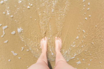 pies de mujer mojándose por una ola en la playa 