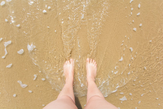 pies de mujer moj&aacute;ndose por una ola en la playa 