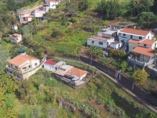 an aerial view of houses and small farms in the steep hillside valley between funchal and madeira with small fields and a road running thought the center