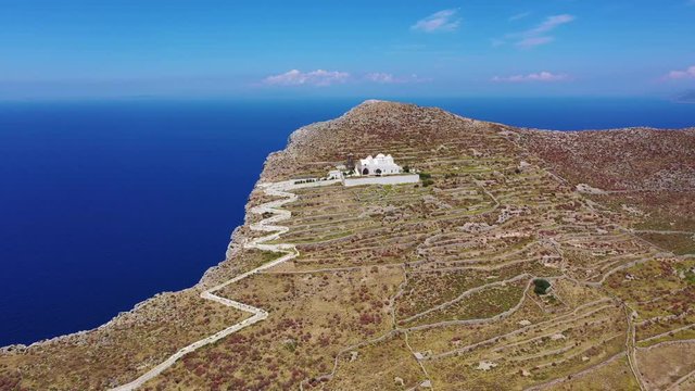Aerial drone video of picturesque uphill church of Panagia built on a steep cliff (Virgin Mary) with stunning views to chora of Folegandros island and deep blue Aegean sea, Cyclades, Greece