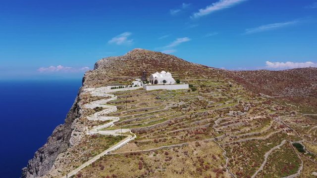 Aerial drone video of picturesque uphill church of Panagia built on a steep cliff (Virgin Mary) with stunning views to chora of Folegandros island and deep blue Aegean sea, Cyclades, Greece