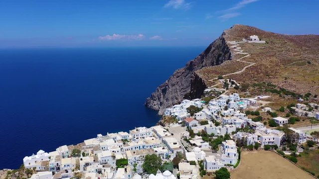 Aerial drone video of iconic and picturesque main village (chora) of Folegandros island featuring castle and built on top of steep hill overlooking the Aegean blue sea, Cyclades, Greece