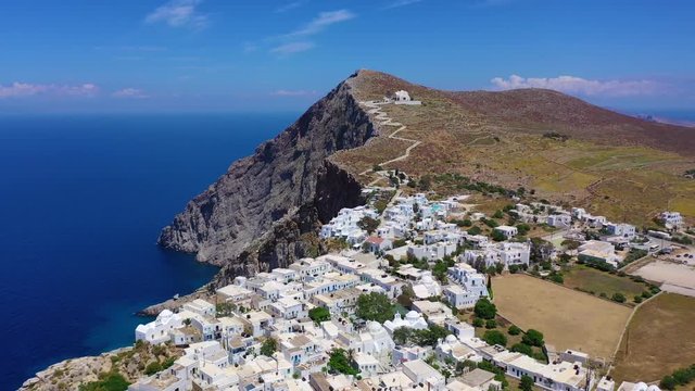Aerial drone video of iconic and picturesque main village (chora) of Folegandros island featuring castle and built on top of steep hill overlooking the Aegean blue sea, Cyclades, Greece