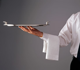 Waiter's arm holds out empty silver tray for service on plain grey background.
