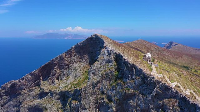 Aerial drone video of picturesque uphill church of Panagia built on a steep cliff (Virgin Mary) with stunning views to chora of Folegandros island and deep blue Aegean sea, Cyclades, Greece