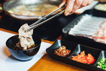 Man pinching boiled well done Kurobuta pork and dipping in ponzu sauce with tong. 