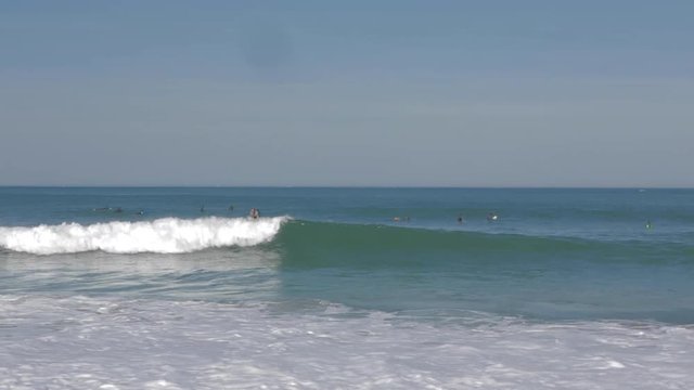 Young man surfing a little wave in sunny atlantic ocean at popular beach in Biarritz, France. 4K. Wide shot.