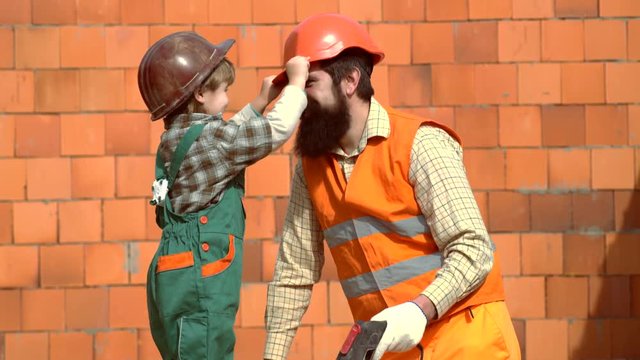 Little son worker erecting a brick wall. Son in hard hat helping his father. Father and Son Building House Together. Son in hard hat helping his father. Child and works.