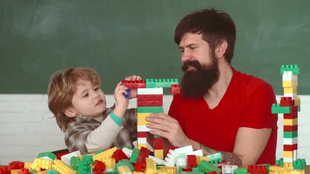 Father and little son with drill perforating wood plank at workshop. Kid boy and father play builders in home. Little son bricklayer building a wall from bricks or stone blocks.