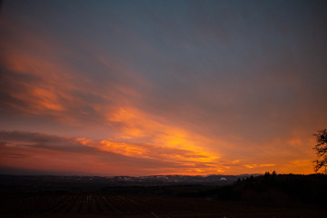 A streak of clouds reflects vivid colors from the setting sun, rich blue and purple above a dark edge of hills.