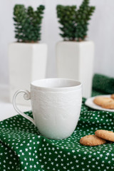 A cup of black tea on a green napkin, homemade cookies, a pair of decorative plants in a pot on the white background.