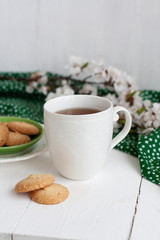 A cup of black tea, homemade cookies, a green napkin and a branch of apricot bloom on the white background.