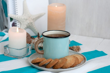 Obraz na płótnie Canvas A hot mug of black tea with homemade cookies on a striped tablecloth, wax candles, decorative starfish, seashell, pile of notebooks on a white background.