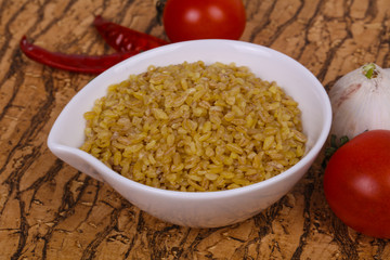 Raw bulgur in the bowl with tomatoes and garlic