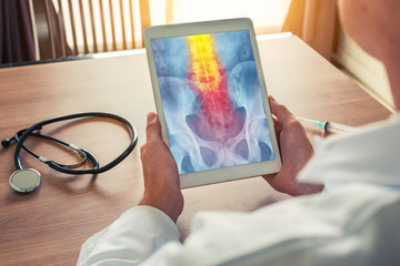 Doctor holding a digital tablet with x-ray of hips with pain on the spine. Stethoscope and syringe...