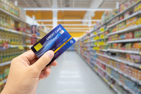 Personal hand holding credit card, with Abstract blurred supermarket view of empty supermarket aisle, defocused blurry background background, cashless concept Electronic money Creating liabilities