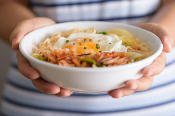 Kimchi noodle spicy soup with egg and vegetables in a bowl holding by hand, Korean food