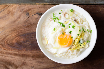 Thai rice soup or soft-boiled rice with pork and egg in the bowl on wooden background - obrazy, fototapety, plakaty