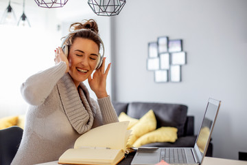 Beautiful woman with headphones over her head and laptop and note book on the table smilling