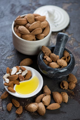 Almond oil and almond nuts over brown stone background, vertical shot, selective focus