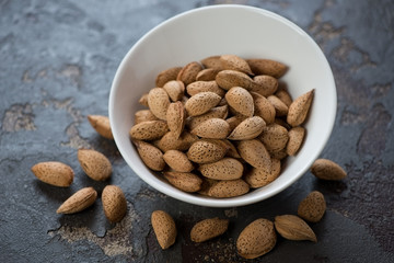 Almond nuts in a white bowl, studio shot on a brown stone background