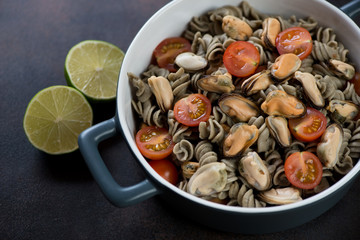 Hemp flour pasta served with mussels and cherry tomatoes in a bowl, studio shot on a brown metal surface