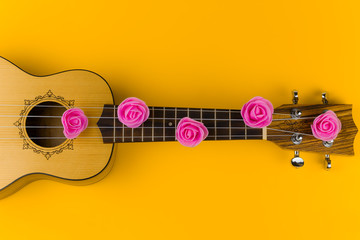 top view of a guitar with rose flowers on the strings lies on  vibrant  yellow  background