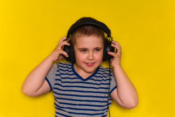 portrait of beautiful cute young boy  with  big black headphones isolated on yellow vibrant background