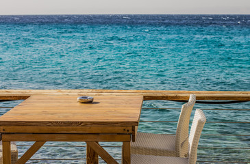 Fototapeta na wymiar cheap face patio on Aegean sea Greece beach with wooden furniture table and chairs, morning breakfast time, copy space