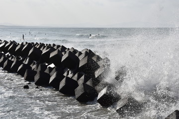 Surfers at Eguchi Hama Seaside Park, Kagoshima, Japan, with crashing wave against tetrapods